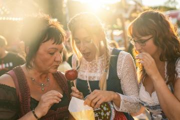 Girlfriends eat roasted almonds together from the paper bag in front of the gingerbread stand at a Bavarian fair or oktoberfest or duld in national costume or Dirndl : Stock Photo or Stock Video Download rcfotostock photos, images and assets rcfotostock | RC Photo Stock.: