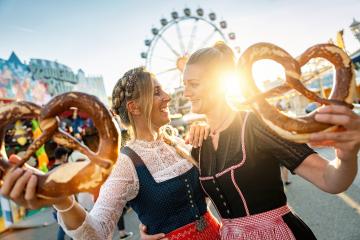 girlfriends look to each other with pretzel or brezen on a Bavarian fair or oktoberfest or duld in national costume or Dirndl- Stock Photo or Stock Video of rcfotostock | RC Photo Stock