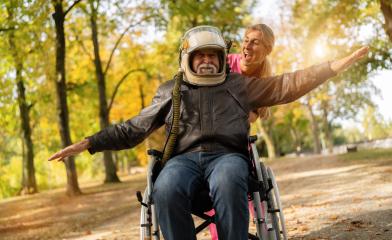 grandfather in an astronaut helmet and leather jacket extends his arms as if flying, with a nurse laughing beside him. Dementia retirement home concept image- Stock Photo or Stock Video of rcfotostock | RC Photo Stock