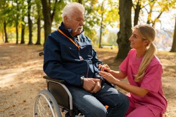 grandpa in wheelchair interacting with caregiver in a park, both smiling, man wearing an SOS button. Dementia retirement home concept image- Stock Photo or Stock Video of rcfotostock | RC Photo Stock