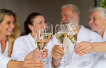 Group of four people in white bathrobes toasting with champagne glasses and celebrating a event in a spa wellness hotel- Stock Photo or Stock Video of rcfotostock | RC Photo Stock