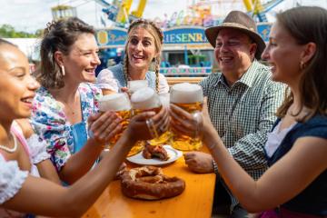 Group of Friends cheerfully toasting with beer mugs at oktoberfest festival on a beer tent table, amusement rides in the background- Stock Photo or Stock Video of rcfotostock | RC Photo Stock