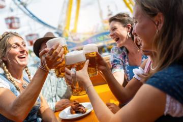 Group of friends laughing and toasting with beer mugs at a oktoberfest festival in munich, amusement park rides in the background- Stock Photo or Stock Video of rcfotostock | RC Photo Stock