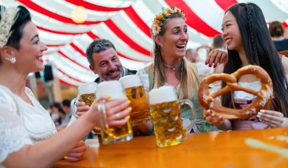 group of people at Oktoberfest happily cheers with frothy beer mugs while holding a large pretzel. They are wearing traditional outfits dirndls and tracht and enjoying the festive atmosphere in munich : Stock Photo or Stock Video Download rcfotostock photos, images and assets rcfotostock | RC Photo Stock.: