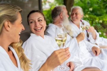 Group of people in white bathrobes laughing and holding champagne glasses celebrating on a lounger at a spa wellness hotel- Stock Photo or Stock Video of rcfotostock | RC Photo Stock