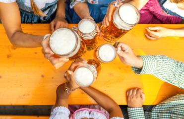 Group of people toasting with large beer steins over a wooden table in a beer tent, wearing traditional Bavarian clothing or tracht at a oktoberfest festival or dult in germany- Stock Photo or Stock Video of rcfotostock | RC Photo Stock