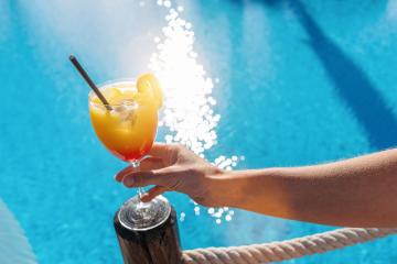 Hand holding a tropical cocktail with a blue pool and sunlight reflecting in the background- Stock Photo or Stock Video of rcfotostock | RC Photo Stock