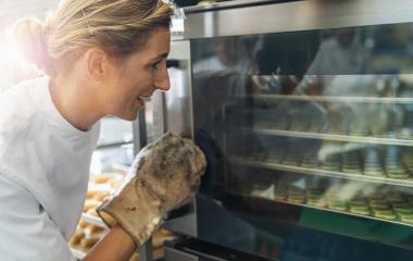 Happy baker woman at the oven controls baking in the oven with glass doors in the bakery : Stock Photo or Stock Video Download rcfotostock photos, images and assets rcfotostock | RC Photo Stock.: