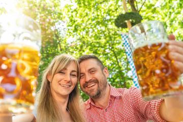 Happy Couple looking and smiling at camera toast beer mugs in a Bavarian beer garden at summer : Stock Photo or Stock Video Download rcfotostock photos, images and assets rcfotostock | RC Photo Stock.: