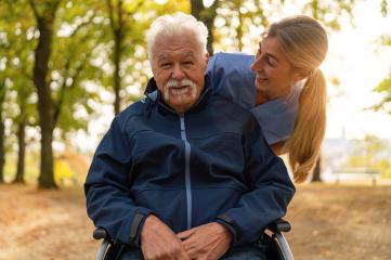 Happy elderly man in a wheelchair with a nurse leaning over him, both smiling in a park with autumn leaves- Stock Photo or Stock Video of rcfotostock | RC Photo Stock