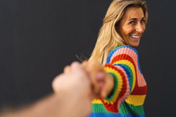 Happy excited woman pulling hand wearing colorful rainbow sweater standing over black background, lgbt celebrating concept image- Stock Photo or Stock Video of rcfotostock | RC Photo Stock