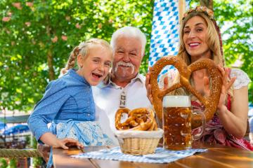 Happy family in proper Tracht holding big pretzel and drinking in Bavarian beer garden at Oktoberfest, folk or beer festival in germany - Stock Photo or Stock Video of rcfotostock | RC Photo Stock
