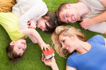 Happy family of four lying on green grass, smiling and playing with a miniature house, symbolizing home ownership, family bonding, and togetherness in a bright and cheerful outdoor setting : Stock Photo or Stock Video Download rcfotostock photos, images and assets rcfotostock | RC Photo Stock.: