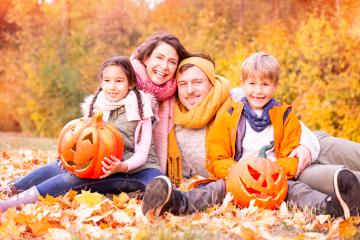 Happy family of four sitting in a park surrounded by autumn leaves, holding carved pumpkins, enjoying a festive fall day with warm scarves and jackets, and vibrant fall foliage in the background : Stock Photo or Stock Video Download rcfotostock photos, images and assets rcfotostock | RC Photo Stock.: