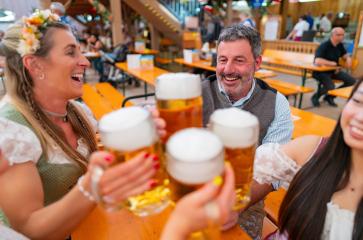 Happy friends in traditional attire toasting with beer steins inside a lively Oktoberfest beer tent with wooden benches, smiling and enjoying the festive atmosphere : Stock Photo or Stock Video Download rcfotostock photos, images and assets rcfotostock | RC Photo Stock.: