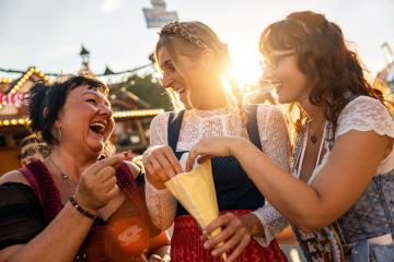 Happy Girlfriends eat roasted almonds together from the paper bag in front of the gingerbread stand at a Bavarian fair or oktoberfest or duld in national costume or Dirndl- Stock Photo or Stock Video of rcfotostock | RC Photo Stock