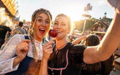 Happy girlfriends eating candy apple on a Bavarian fair or oktoberfest or duld in national costume or Dirndl in germany  : Stock Photo or Stock Video Download rcfotostock photos, images and assets rcfotostock | RC Photo Stock.: