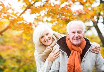Happy senior couple enjoying a warm autumn day outdoors with colorful foliage in the background, expressing love, warmth, and companionship in cozy scarves and sweaters- Stock Photo or Stock Video of rcfotostock | RC Photo Stock