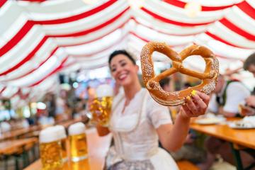 happy woman at Oktoberfest or dult holds a large pretzel in one hand and a beer mug in the other, wearing a traditional outfit. The vibrant tent background adds to the festive and joyful atmosphere : Stock Photo or Stock Video Download rcfotostock photos, images and assets rcfotostock | RC Photo Stock.: