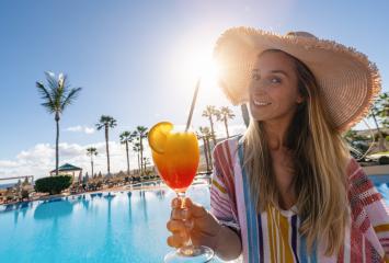 Happy woman in a straw hat holding a tropical cocktail at a poolside, with palm trees and blue sky in the background at caribbean island hotel - Stock Photo or Stock Video of rcfotostock | RC Photo Stock