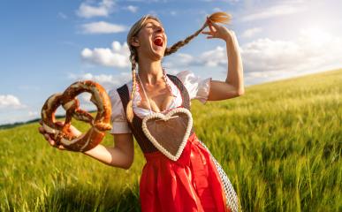 Happy woman in Bavarian dirndl with a gingerbread heart, laughing and holding a pretzel in a wheat field celebrating Oktoberfest or dult festival in munich.- Stock Photo or Stock Video of rcfotostock | RC Photo Stock
