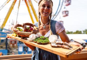 Happy woman in traditional Bavarian dress serving a variety of German foods at a fair dult or oktoberfest in germany- Stock Photo or Stock Video of rcfotostock | RC Photo Stock