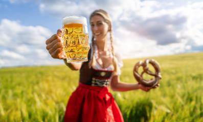 Happy woman in traditional Bavarian tracht showing a beer mug and pretzel in a wheat field celebrating Oktoberfest festival in munich.- Stock Photo or Stock Video of rcfotostock | RC Photo Stock