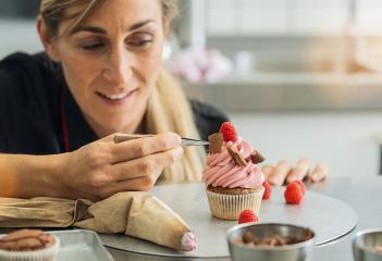 Happy women in pastry bakery as confectioner draped a piece of chocolate on a muffin topping with tweezers : Stock Photo or Stock Video Download rcfotostock photos, images and assets rcfotostock | RC Photo Stock.: