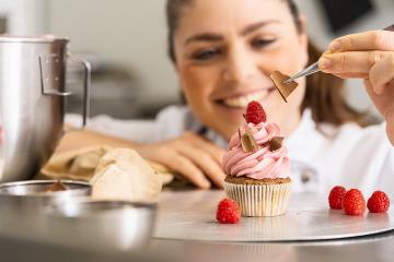 happy women in pastry bakery as confectioner draped pieces of chocolate on a muffin topping with tweezers : Stock Photo or Stock Video Download rcfotostock photos, images and assets rcfotostock | RC Photo Stock.: