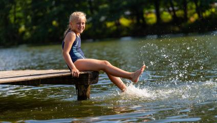 Happy young girl splashing water with her feet while sitting on a wooden dock by a lake at summer- Stock Photo or Stock Video of rcfotostock | RC Photo Stock