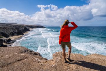 Hiker in red jacket looking out at the ocean waves from a cliff on a sunny day : Stock Photo or Stock Video Download rcfotostock photos, images and assets rcfotostock | RC Photo Stock.: