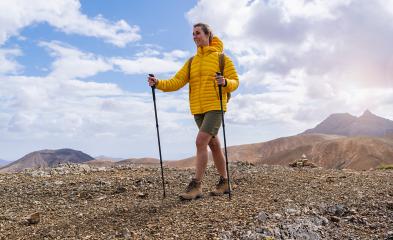 Hiker in yellow jacket with trekking poles on a rocky mountain trail, mountains in the back : Stock Photo or Stock Video Download rcfotostock photos, images and assets rcfotostock | RC Photo Stock.: