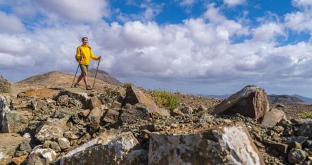 Hiker in yellow on rocky mountain terrain with cloudy blue sky in the background- Stock Photo or Stock Video of rcfotostock | RC Photo Stock