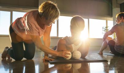 Instructor assisting yoga student with posture with massage ball, sunny studio, reflective floor- Stock Photo or Stock Video of rcfotostock | RC Photo Stock
