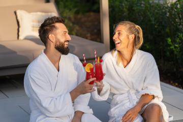 joyful couple in white bathrobes clinking glasses with red drinks, outdoors at golden hour at a hotel- Stock Photo or Stock Video of rcfotostock | RC Photo Stock