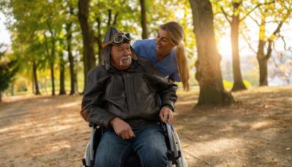 Joyful elderly man in aviator gear looking up while being pushed in a wheelchair by a smiling nurse in a sunlit park. Dementia retirement home concept image- Stock Photo or Stock Video of rcfotostock | RC Photo Stock