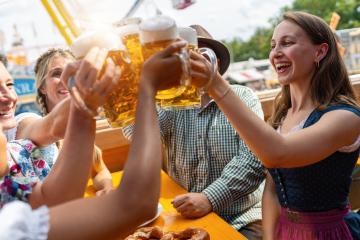 Joyful friends clinking beer mugs at a oktoberfest or dult festival beer tent table, amusement rides and blue sky in the background- Stock Photo or Stock Video of rcfotostock | RC Photo Stock