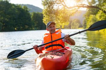 Joyful senior man in an orange life vest paddling a red kayak on a river, surrounded by lush greenery. Kayak Water Sports concept image- Stock Photo or Stock Video of rcfotostock | RC Photo Stock