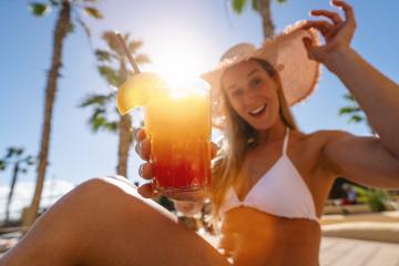 joyful woman in a white bikini and straw hat holding a colorful cocktail, with palm trees in the background at caribbean island hotel - Stock Photo or Stock Video of rcfotostock | RC Photo Stock