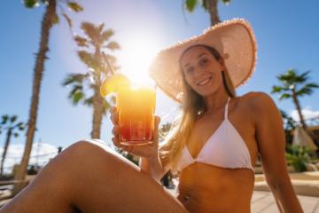 joyful woman in a white bikini and straw hat toasts with a tropical cocktail, palm trees in the background at caribbean island hotel - Stock Photo or Stock Video of rcfotostock | RC Photo Stock