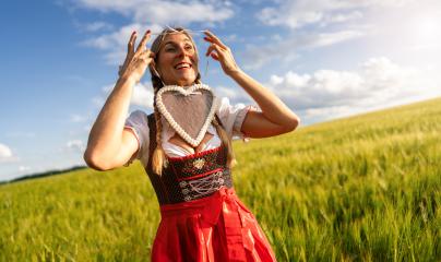 Joyful woman in Bavarian costume placing a gingerbread heart around her head, in a wheat field celebrating Oktoberfest in munich, with copyspace for your individual text.- Stock Photo or Stock Video of rcfotostock | RC Photo Stock