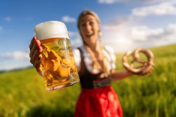 Joyful woman in Bavarian dress presenting a beer and pretzel outdoors in a field´ready for Oktoberfest festival in munich, germany- Stock Photo or Stock Video of rcfotostock | RC Photo Stock