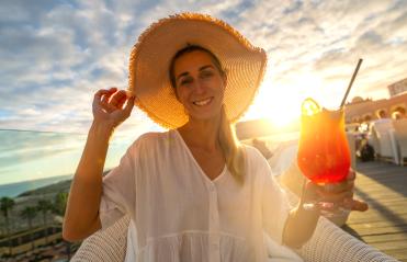 Joyful woman in straw hat offering a cocktail at tropical beach hotel with sunset in the background- Stock Photo or Stock Video of rcfotostock | RC Photo Stock