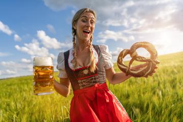 Joyful woman in traditional Bavarian dress holding beer and pretzel in a sunny field ready for Oktoberfest festival in munich, germany- Stock Photo or Stock Video of rcfotostock | RC Photo Stock