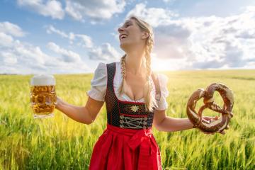 joyful woman in traditional Bavarian dress holds beer and pretzel in a sunny wheat field celebrating Oktoberfest in munich.- Stock Photo or Stock Video of rcfotostock | RC Photo Stock