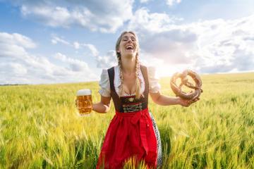 Joyful woman in traditional Bavarian dress with beer and pretzel in a field celebrating Oktoberfest or dult festival in munich.- Stock Photo or Stock Video of rcfotostock | RC Photo Stock