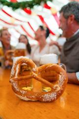 large pretzel in the foreground with several mugs of beer in the background, and friends celebrating at Oktoberfest and dult under colorful striped tent in munich : Stock Photo or Stock Video Download rcfotostock photos, images and assets rcfotostock | RC Photo Stock.: