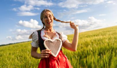 Laughing woman in Bavarian costume playing with her braid and holding a gingerbread heart in a wheat field celebrating Oktoberfest in munich, with copyspace for your individual text.- Stock Photo or Stock Video of rcfotostock | RC Photo Stock