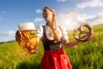 Laughing woman in Bavarian tracht holding a beer and pretzel in a sunny field celebrating Oktoberfest or dult festival in munich.- Stock Photo or Stock Video of rcfotostock | RC Photo Stock