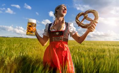 Laughing woman in traditional Bavarian dress holding beer and pretzel in a sunny wheat field celebrating Oktoberfest or dult festival in munich.- Stock Photo or Stock Video of rcfotostock | RC Photo Stock